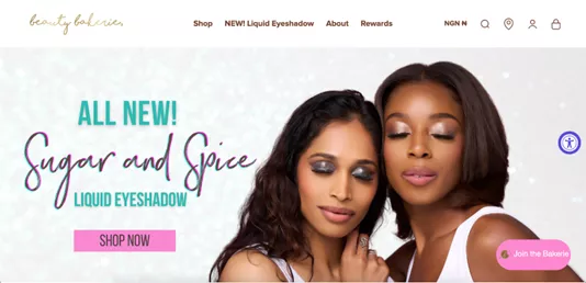 Shopify stores: Two women with shimmery eye makeup pose closely together in front of a sparkling background. Text reads “All New! Sugar and Spice Liquid Eyeshadow.” There is a pink “Shop Now” button below the text.