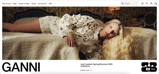 Shopify stores: A person with long blonde hair in a white crocheted outfit lounges on a vintage bed in a floral wallpapered room. The text reads “GANNI” and “Just Landed: Spring/Summer 2026 Collection.”.