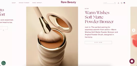 Shopify stores: A makeup brush rests on an open compact of bronzer. The text beside it reads Warm Wishes Soft Matte Powder Bronzer and describes it as designed for a seamless, natural look. The site is branded Rare Beauty.
